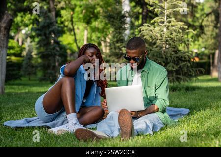 Viele Studenten, die mit einem Notebook beschäftigt sind, Filme ansehen und im Park im Internet surfen Stockfoto