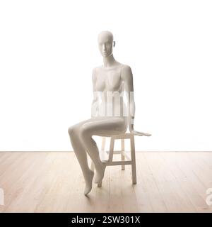 Die weiße weibliche Sitzpuppe ist elegant auf einem Hocker vor einem weißen Hintergrund mit Holzboden positioniert. Stockfoto