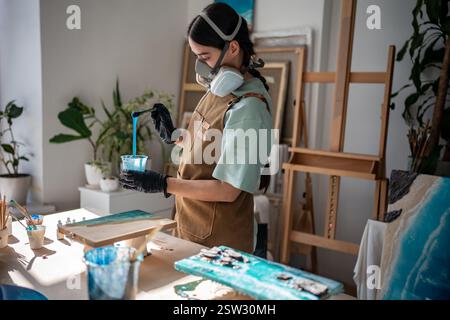 Handwerker in Atemschutzgeräten rührt Epoxidharz mit Pigment um, um Konsistenz für die Lackierung in der Werkstatt zu schaffen Stockfoto