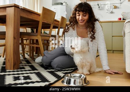 Eine junge Frau sitzt auf dem Boden und interagiert warm mit ihrem kleinen Hund an einer Schüssel. Stockfoto