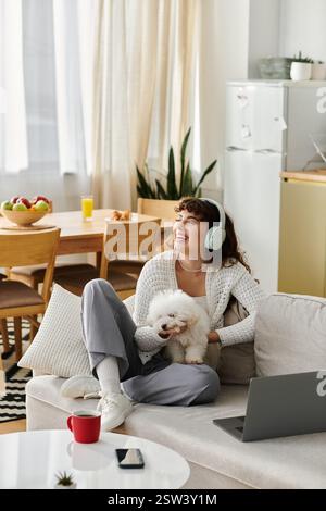 Eine junge Frau entspannt sich auf einer Couch mit Kopfhörern und kuschelt ihren Welpen in einem fröhlichen Zimmer. Stockfoto