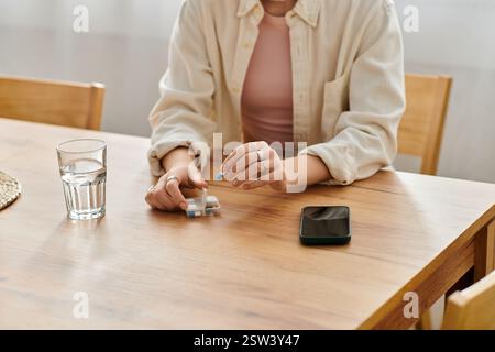 Eine junge Frau sitzt an einem Holztisch und reflektiert, während sie Medikamente und ein Telefon in der Nähe hält. Stockfoto