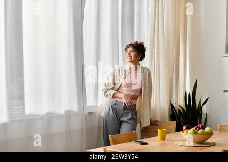 Eine junge Frau lehnt sich an einen Holztisch, lächelt sanft, während sie auf das Morgenlicht blickt. Stockfoto