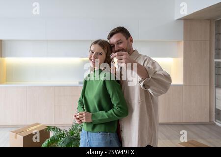 Fröhliche Familie umarmt sich, hält Schlüssel für die neue Wohnung nach dem Umzug. Umzug für Paare, Hausvermietung Stockfoto