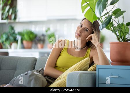 Porträt einer Frau auf dem Sofa unter Pflanzen, die in die Kamera blicken, mit ruhigem, selbstbewusstem Ausdruck im Gesicht Stockfoto