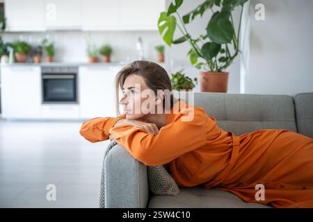 Die nachdenkliche träumende Frau liegt auf dem Sofa und blickt auf das Fenster. Genießen Sie Ruhe für eine ruhige Entspannung. Stockfoto