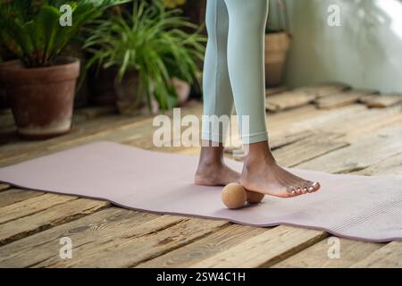 Afrikanerin steht auf der Turnmatte mit Massageball, um Spannfüße auszurollen. Verbringen Sie Zeit für Selbstpflege Stockfoto