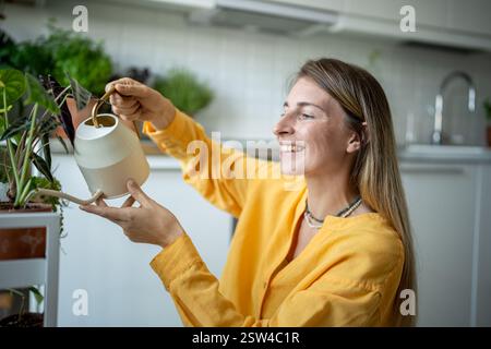 Fröhliche Pflanzenliebhaberin, die Hausaufgaben macht, sich um Topfpflanzen kümmert, Blumen tränkt Stockfoto