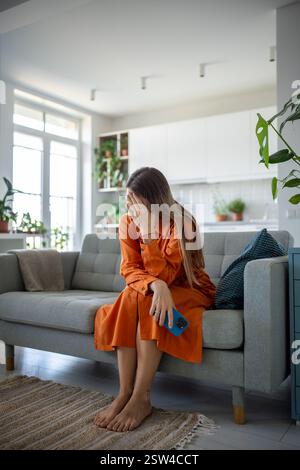 Unglückliche traurige Frau in schwieriger Lage zu Hause auf der Couch mit Smartphone zu sitzen, erhielt schlechte Nachrichten Stockfoto