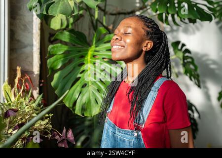 Lächelnde schwarze Frau im Innengarten. Afroamerikaner fröhliches Mädchen gegen Pflanzenblätter Stockfoto