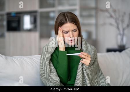 Frau fühlt sich unwohl, hat Symptome von Grippe, Virus, leidet an Kopfschmerzen Blick auf Thermometer Stockfoto