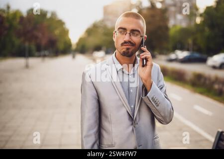 Porträt eines verzweifelten Geschäftsmannes, der am Telefon spricht. Junger Geschäftsmann, der auf der Straße steht und ein Smartphone benutzt. Stockfoto