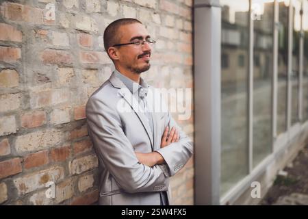 Porträt eines jungen Geschäftsmannes, der vor einer Ziegelmauer steht, wegblickt und denkt. Stockfoto