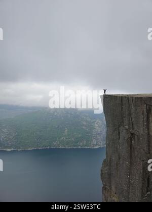 Majestätischer Blick auf den Fjord von den Preikestolen Cliffs in Norwegen mit Abenteurer bei Sonnenuntergang Stockfoto