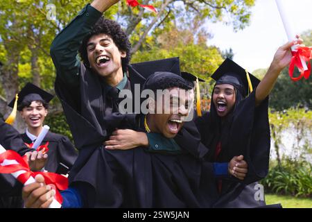 Absolventen verschiedener Studenten, die Mützen und Kleider tragen, feiern im Garten und fühlen sich fröhlich. Abschluss, Ausbildung, Feier, Erfolg, Erfolg, UN Stockfoto