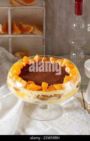 Tiramisu-Dessert mit Mascarponcreme und Zitronen-Mandarinen-Quark. Traditionelles italienisches Dessert, dekoriert mit Kakao, Mandarinenscheiben und Rosmarin auf einem li Stockfoto