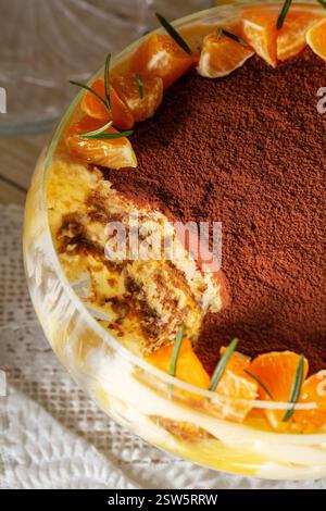 Tiramisu-Dessert mit Mascarponcreme und Zitronen-Mandarinen-Quark. Traditionelles italienisches Dessert, dekoriert mit Kakao, Mandarinenscheiben und Rosmarin auf einem li Stockfoto