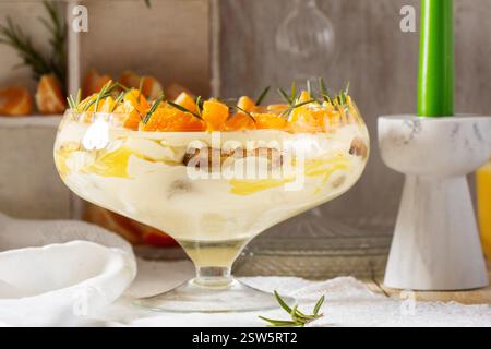 Tiramisu-Dessert mit Mascarponcreme und Zitronen-Mandarinen-Quark. Traditionelles italienisches Dessert, dekoriert mit Kakao, Mandarinenscheiben und Rosmarin auf einem li Stockfoto