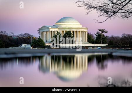 WASHINGTON DC – das Thomas Jefferson Memorial wird in rosafarbenem Licht in der Abenddämmerung beleuchtet, während es sich auf den stillen Gewässern des Tidal Basin reflektiert. Das 1943 geweihte neoklassizistische Denkmal erzeugt ein Spiegelbild auf der Wasseroberfläche. Rosafarbene Farbtöne des Sonnenuntergangs tauchen die weiße Marmorstruktur in ein warmes Licht am Abendhimmel. Stockfoto