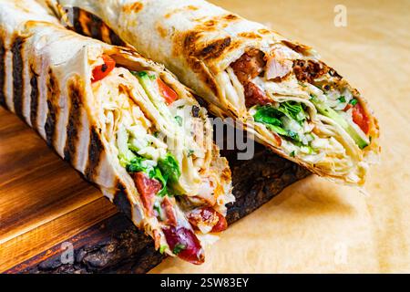 Zwei gegrillte Wraps zeigen eine bunte Mischung aus gegrilltem Huhn, frischem Gemüse und Saucen. Die warmen Tortillas sind perfekt getoastet, was sie zu einem A macht Stockfoto