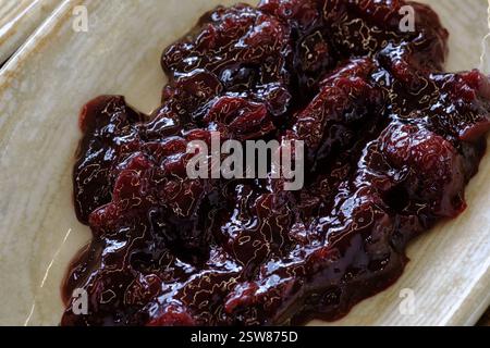 Eine Nahaufnahme dunkler, glänzender Fruchtkonserven, möglicherweise Kirsch oder Pflaume in einem flachen Gericht reichhaltig und dekadent Stockfoto