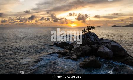 Sonnenuntergang über dem Meer mit Wellen, die gegen ein felsiges Ufer brechen und weißen Schaum erzeugen. Seychellen, Mahe. Stockfoto