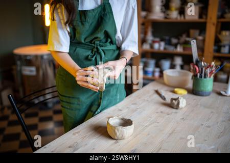 Frauen Töpferhände Formen eine weiße Tonschale an einem kerzenbeleuchteten Holztisch im Keramikwerkstattstudio Stockfoto
