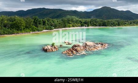 Eine ruhige Küstenlandschaft mit felsigem Ufer, türkisfarbenem Wasser und fernen grünen Hügeln unter hellem Himmel. Stockfoto