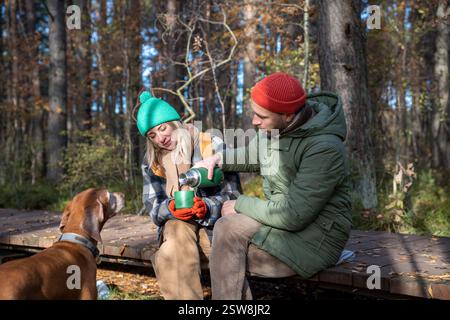Ehepaar mittleren Alters mit Hund, der Tee trinkt, sitzt auf Ökotrop im Herbstpark Nordskandinavien. Stockfoto