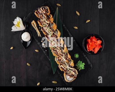Tempura Maki Sushi-Brötchen mit Sesamsamen und Sauce auf schwarzem Steinteller Stockfoto