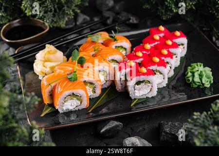 Köstliches Sushi-Brötchen-Set, serviert auf schwarzem Teller, präsentiert auf dunklem Hintergrund Stockfoto