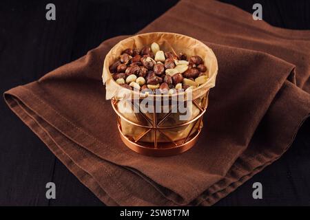 Kupferkorb, der mit gerösteten Erdnüssen überfüllt ist und auf brauner Serviette sitzt Stockfoto