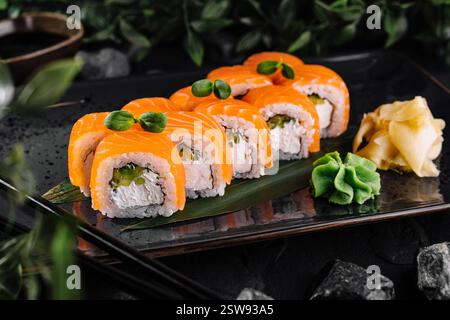 Philadelphia-Sushi-Brötchen, die mit Lachs bedeckt sind und mit Grünzeug dekoriert sind und auf schwarzem Teller serviert werden Stockfoto