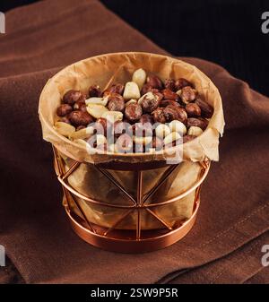 Kupferkorb, der mit gerösteten Erdnüssen überfüllt ist und auf brauner Serviette sitzt Stockfoto