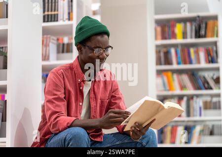Interessierter afroamerikanischer Student liest Buch in der Universitätsbibliothek, studiert für die Prüfung. Stockfoto
