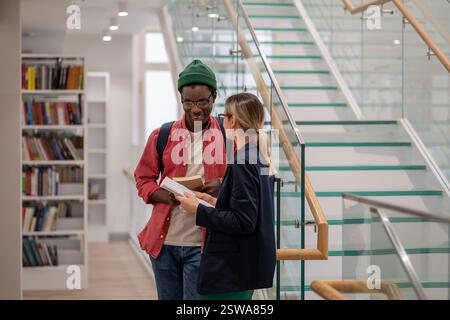 Lächelnde afroamerikanische Studentenkommunikation mit europäischer Freundin in der Universitätsbibliothek Stockfoto