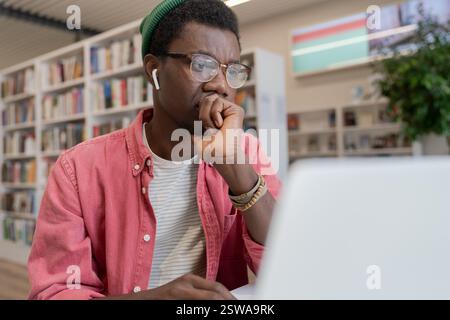 Fokussierter afroamerikanischer Schüler, der sich Online-Kurs auf einem Laptop in der Bibliothek ansieht Stockfoto