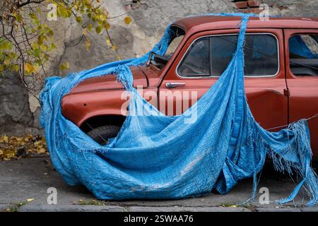 Verlassenes Retro-Fahrzeug mit zerbrochenem Glas, bedeckt mit zerrissener blauer Markise, um Metallkorrosion zu verhindern Stockfoto