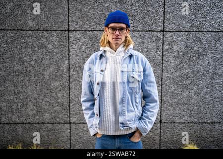 Blonder, langhaariger Kerl, skandinavischer androgyner Auftritt in Brille, die auf der Straße steht. Stockfoto