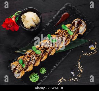 Tempura Maki Sushi-Brötchen mit Sesamsamen und Unagi-Sauce auf schwarzem Steinteller Stockfoto