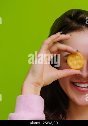 Eine junge Frau, die einen Salzcracker vor den Augen hält und lächelt Stockfoto