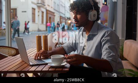 Indischer arabischer Mann männlicher Geschäftsmann Kunde Geschäftsmann Online-Arbeit im Café Fernunterricht mit Geräten Laptop Telefon Musik in Kopfhörern hören Stockfoto