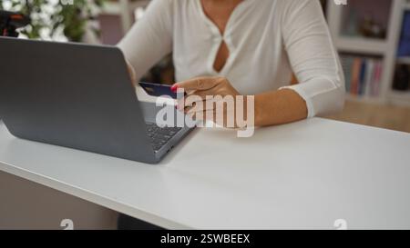 Frau, die zu Hause online mit Laptop und Kreditkarte einkaufen möchte, zeigt Hände mittleren Alters und Erwachsene in Inneneinrichtung Stockfoto