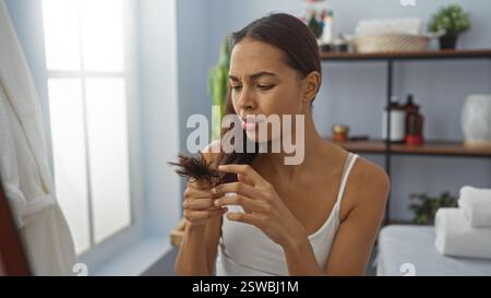 Junge Frau, die Spliss im Wellnessraum des Schönheitssalons untersucht und sich auf die Haargesundheit in gemütlichem Spa-Interieur konzentriert. Stockfoto