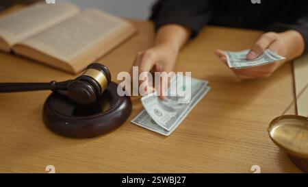 Weibliche Hände, die uns Dollarscheine neben dem Hammer eines Richters in einem Büro zählen, was auf Konzepte von Recht, Gerechtigkeit, Bestechung und Korruption hinweist. Stockfoto
