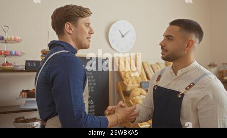 Zwei Bäcker schütteln die Hände in einem Backwareninnenraum mit Brot und Desserts im Hintergrund Stockfoto