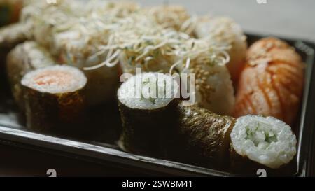 Nahaufnahme verschiedener Sushi-Rollen und Sashimi auf einem schwarzen Tablett auf einer Betonoberfläche Stockfoto