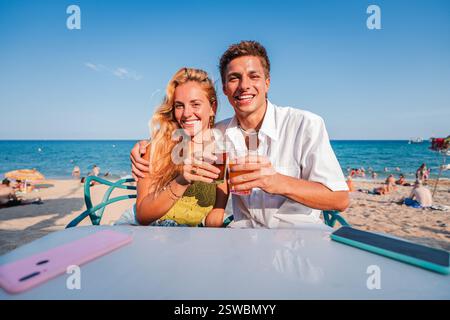 Fröhliche Paare, die an einem sonnigen Strand mit Drinks anstoßen, erfrischende Getränke genießen und den perfekten Moment an der Küste unter einem klaren blauen Himmel voller warmer Sonne und Lachen festhalten. Hochwertige Fotos Stockfoto