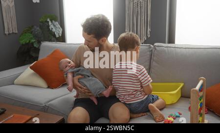Vater verbindet sich mit seinem Baby, während der ältere Sohn im Wohnzimmer spielt und einen Moment der Familienliebe und des Zusammenlebens in einem gemütlichen Wohnraum festhält. Stockfoto