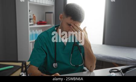 Die junge hispanische Krankenschwester im Klinikzimmer schaut gestresst an seinem Schreibtisch mit grünen Peelings und medizinischen Geräten herum. Stockfoto